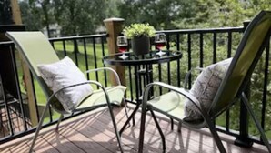Eine Holzterrasse mit zwei grünen Stühlen und einem kleinen Tisch mit einem Blumentopf und zwei Weingläsern.
