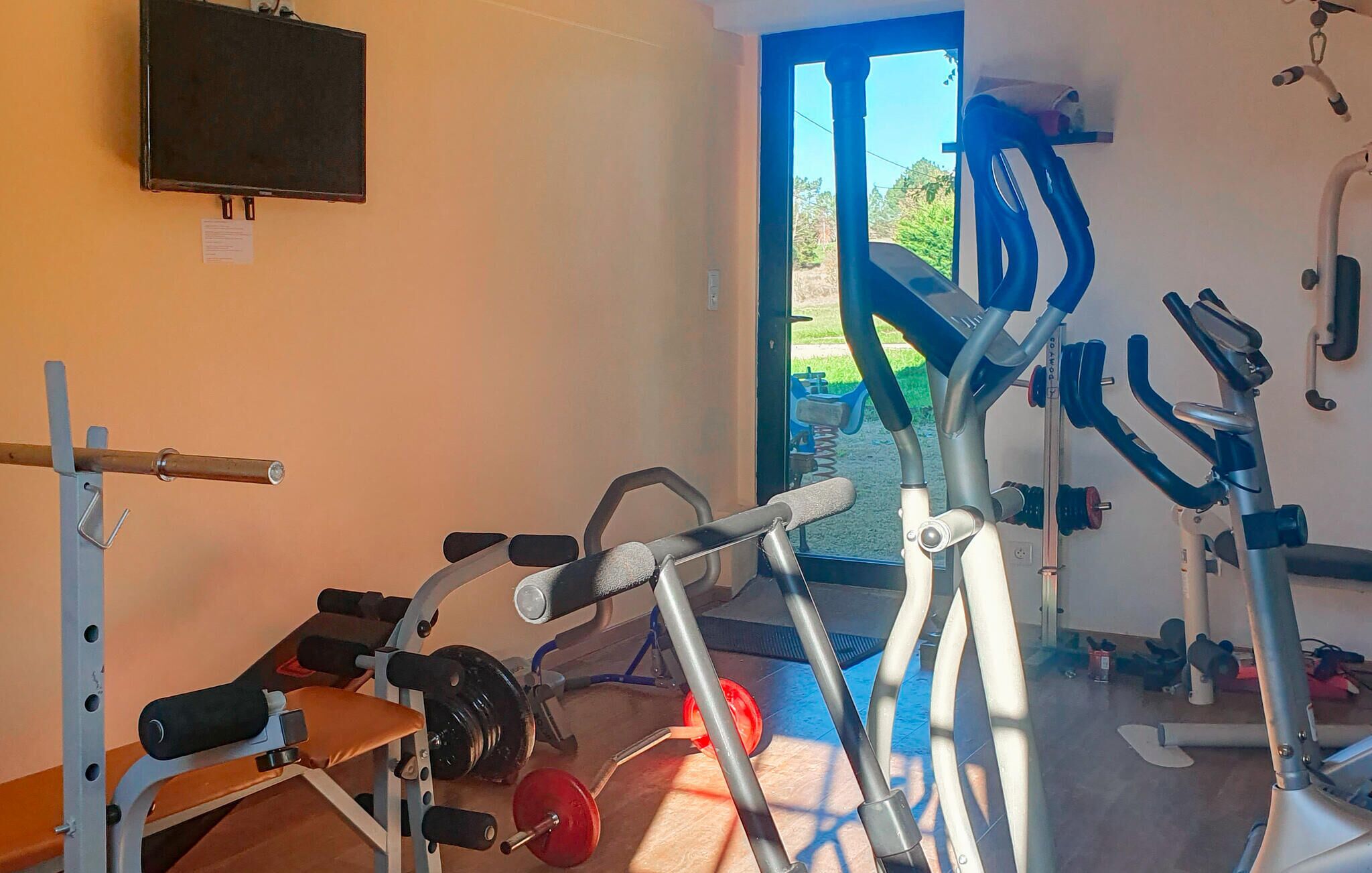A gym with exercise equipment, a television on the wall, and a door leading outside.