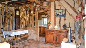 Une pièce rustique avec des poutres apparentes, une table en bois recouverte d’une nappe blanche, un buffet en bois et une horloge murale.