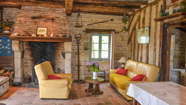 Une pièce rustique avec une cheminée en briques, des canapés en cuir jaune, une petite table ronde ornée d’un vase et un plafond en bois.