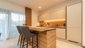 Een moderne keuken met een houten kookeiland, barstoelen en een uitzicht op de omgeving door grote ramen.