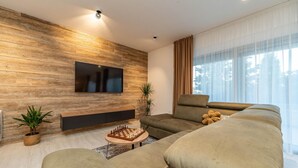 Een moderne woonkamer met een houten wand, een flatscreen televisie, een bank en een schaakkastje.