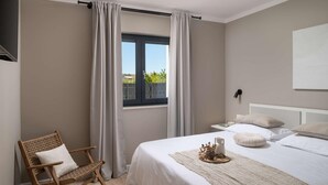 Een slaapkamer met een bed, een stoel, een raam met gordijnen, een nachtkastje en een wandlamp.
