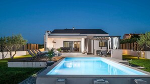 Een modern huis met een zwembad, terras en een verzorgde tuin.