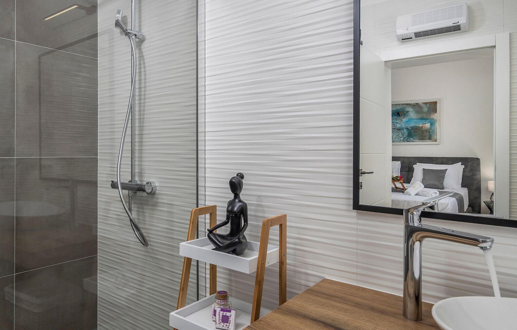 Een moderne badkamer met een douche, een wastafelmeubel en een spiegel die een slaapkamer weerspiegelt.