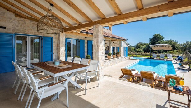 Un espacio al aire libre techado con piscina, mesa, sillas y sombrillas.