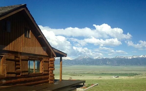 Situated in a vast landscape, this cabin offers a sheltered porch area and breathtaking views of snow-capped mountains.