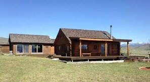 Situated in a serene grassy area, this cabin features a cozy porch with a bench and a prominent chimney.