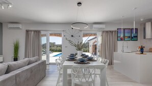 A modern kitchen with white cabinetry, a dining area with a white table and chairs, and a view of the outdoor swimming pool. - Beautiful home in Sukosan with WiFi (Sukosan)