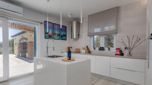 A modern kitchen with a central island, a built-in sink, and a stainless steel range hood. There are framed artworks above the island and a window with a view of the outside. - Beautiful home in Sukosan with WiFi (Sukosan)