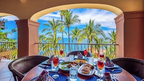 Une table à manger dressée avec des assiettes, des verres et une vue sur un paysage tropical.