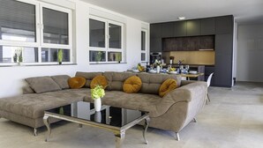 A modern living room with a sectional sofa, a glass coffee table, and a kitchen area with a dining table set for four. - Cozy home in Nin with house sea view (Nin)
