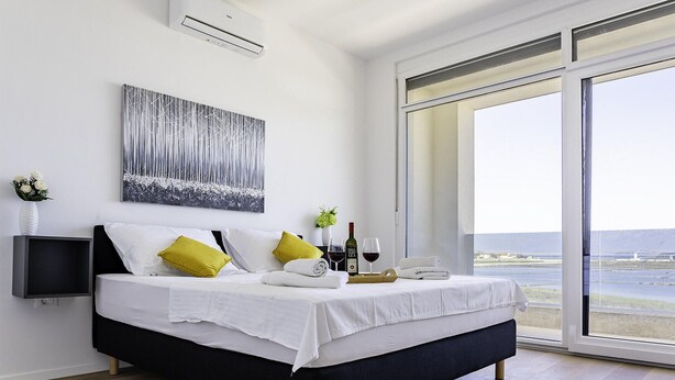 A bedroom with a bed, a bedside table, a wall-mounted air conditioner, a window with a view, and a painting on the wall. - Cozy home in Nin with house sea view (Nin)