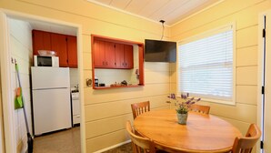 A compact kitchen with a refrigerator, microwave, and red cabinets. There is a dining table with chairs and a potted plant. - Big Rock Resort (June Lake)