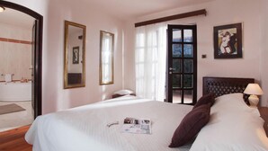 Ein Hotelzimmer mit einem großen Bett, einem Nachttisch mit Lampe, einer Tür, die nach draußen führt, und einem gerahmten Bild an der Wand.