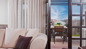 Ein modernes Wohnzimmer mit einer Couch, einem Esstisch mit Stühlen und einer Glastür, die auf eine Terrasse im Freien führt.