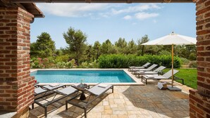 A pool area with lounge chairs and a table, surrounded by a brick wall and greenery.