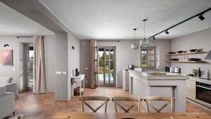 A modern kitchen with a central island, a dining area with a wooden table, and a view of a swimming pool through a glass door.