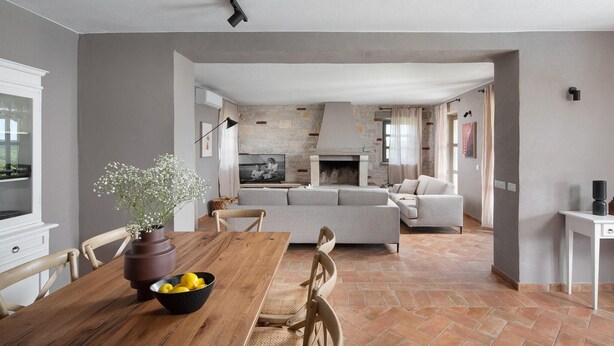 A modern living room with a fireplace, a dining area with a wooden table and chairs, and a kitchen visible in the background.