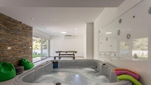 Een moderne spa-ruimte met een stenen hottub, groene loungestoelen en een houten bankje.