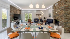 Een moderne eethoek met een glazen tafel, oranje kussens en een open haard.