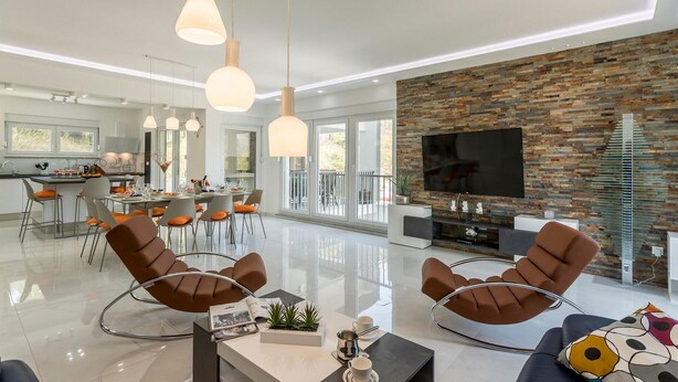 Een moderne woonkamer met een stenen accentmuur, een flatscreen televisie en een eethoek met een glazen tafel en stoelen.