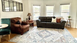 Ein Wohnzimmer mit einem braunen Sessel, einem dunkelgrauen Sofa, einem gemusterten Teppich und einem kleinen runden Tisch.