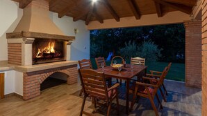 Eine Terrassengrundstück mit Kamin aus Ziegeln, einem Holztisch und Stühlen.