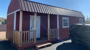 A small, single-story building with a red exterior and a metal roof. It has a front porch with a wooden railing and a door. - The Wild West's Best Kept Secret  (Hurricane)