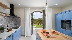 A modern kitchen with blue cabinets, a wooden countertop, and a view of a garden through a glass door. - Lovely home in Karojba with sauna (Karojba)