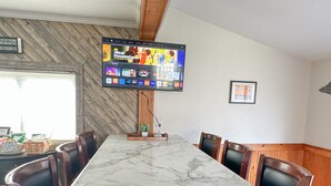 Restaurante com mesa de tampo em mármore, cadeiras de couro preto, televisão de tela plana na parede e parede de destaque em madeira.