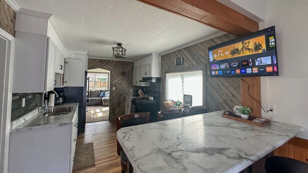 Cozinha moderna com bancada de mármore, vigas de madeira no teto e uma televisão de tela plana exibindo um serviço de streaming.