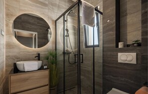 Ein modernes Badezimmer mit rundem Spiegel, Waschbecken mit Handtuch, einer Duschkabine und einem Fenster.