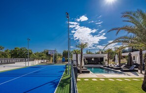 A pool area with a tennis court, a pool, and a building with a covered patio.