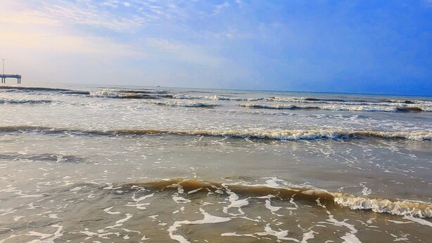Ein Strand mit Wellen und einem Pier im Hintergrund.