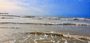 A beach with waves and a pier in the background. - Port A 2BR/2BA Duplex – Fenced Yard, Dogs OK, Boat Parking, Cart Zone (Port Aransas)