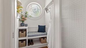 A white interior with a bench, baskets, and a wall-mounted circular window.