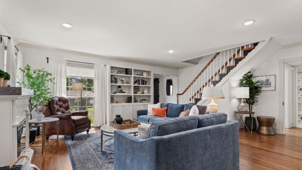 A spacious living room with a blue sofa, a leather armchair, and a staircase leading to a second floor.