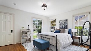 A bedroom with a large bed, a desk, and a chair, with a view of the outdoors through large windows.
