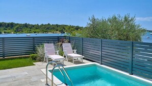A pool with two white lounge chairs and a metal ladder, surrounded by a dark fence, with a view of boats on a lake and trees in the background. - 6 bedroom stunning home in Medulin (Medulin)
