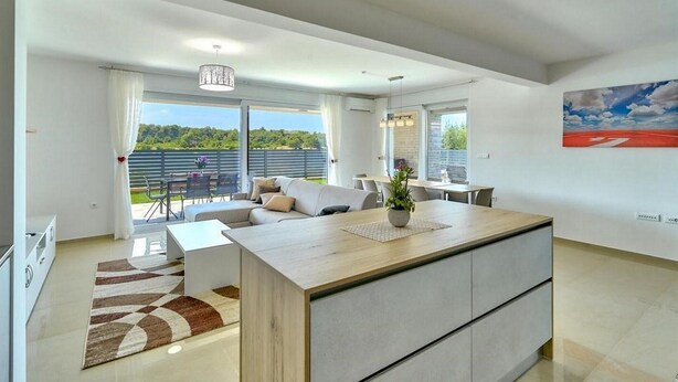 A modern living room with a large island, a sofa, and a dining area. There is a view of greenery outside. - 6 bedroom stunning home in Medulin (Medulin)