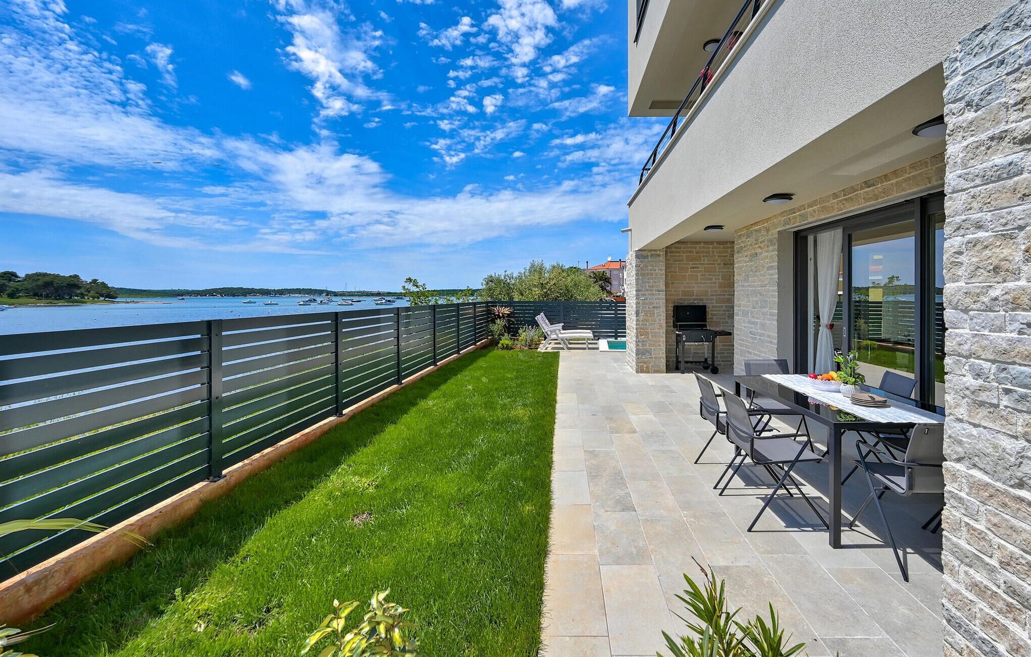 Een modern terras buiten, met een stenen muur, een zwembad en uitzicht op het water.
