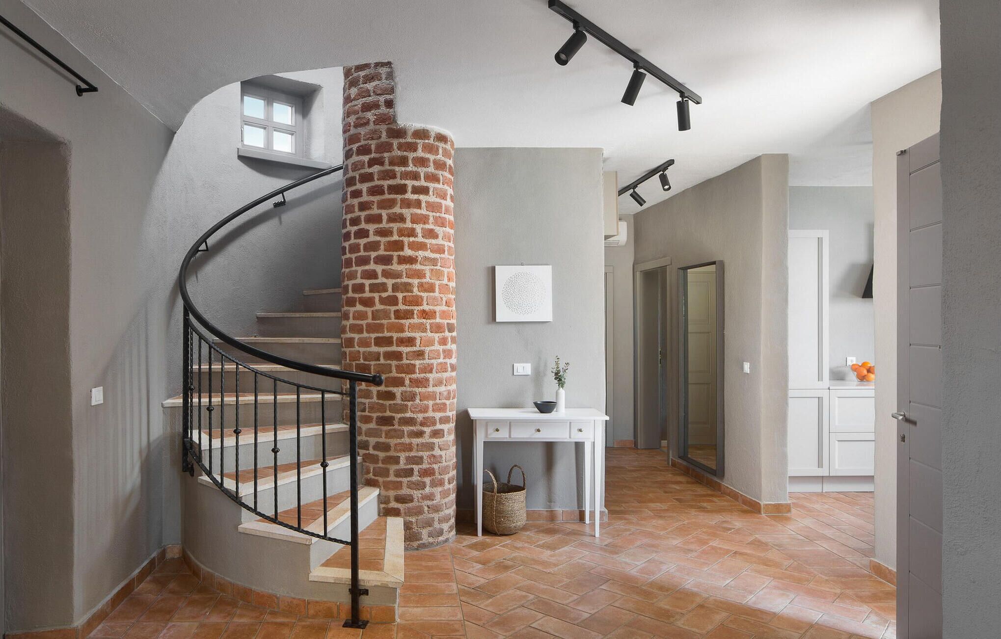 A spiral staircase with a brick column, a white console table with a vase and a basket, and a door leading to another room.