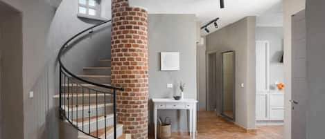 A spiral staircase with a brick column, a white console table with a vase and a basket, and a door leading to another room.