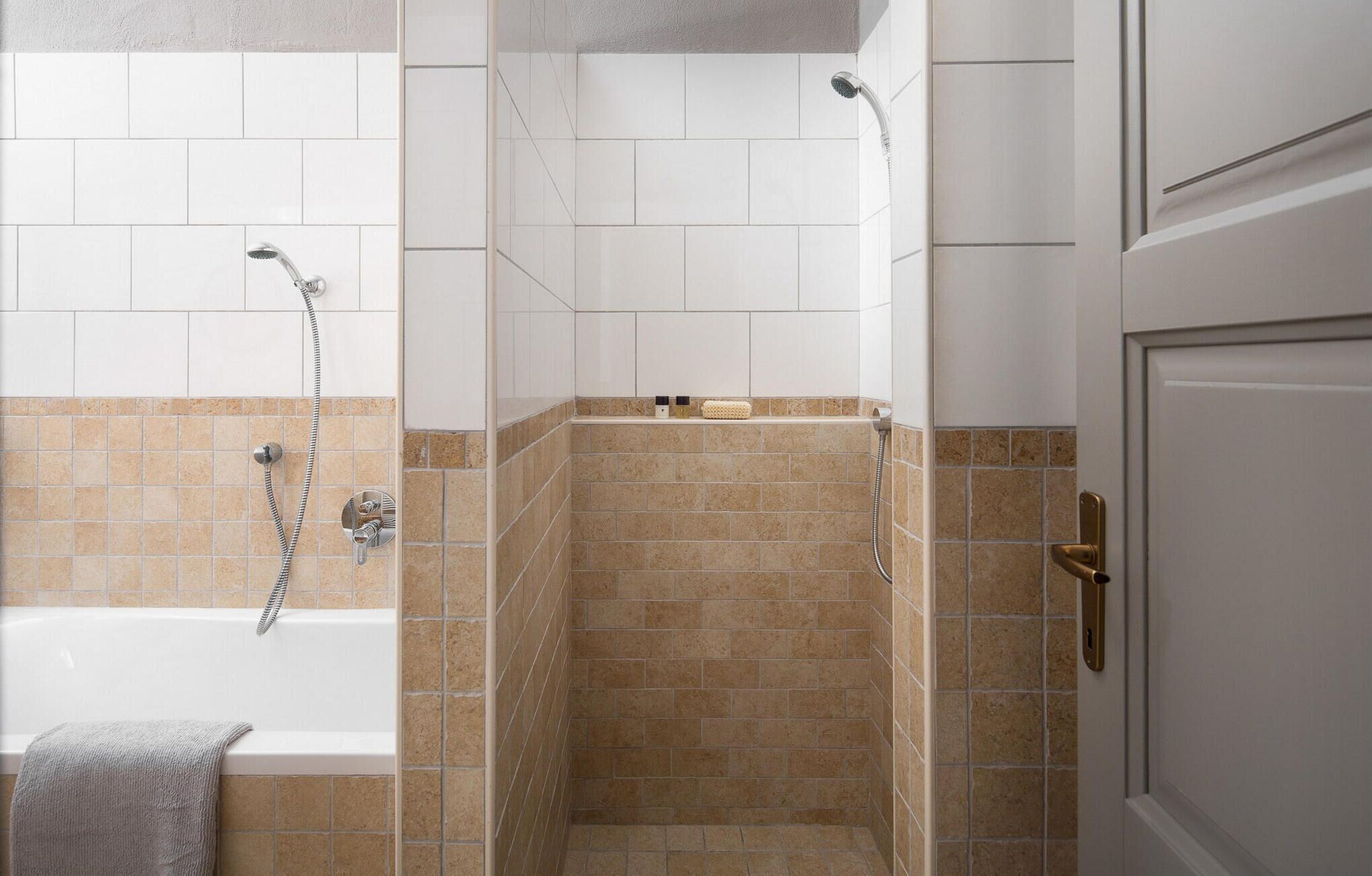 Una ducha a nivel del suelo con bañera, azulejos color crema y blanco, y una toalla sobre la bañera.