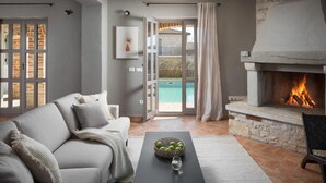 Un soggiorno con camino, una piscina visibile tramite una porta vetrata e un divano con cuscini.