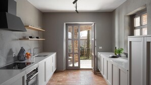 Una cucina stretta con mobili bianchi, forno integrato, lampadario e vista su uno spazio esterno attraverso una porta vetrata.
