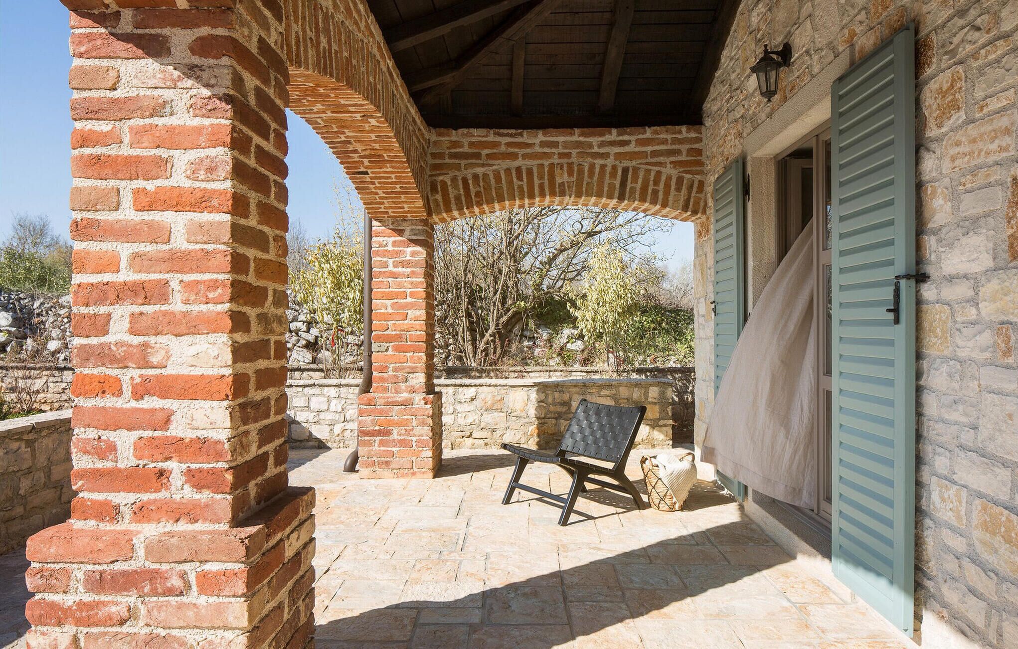 A covered outdoor area with a brick archway, a stone wall, and a bench.