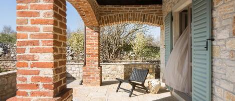 A covered outdoor area with a brick archway, a stone wall, and a bench.