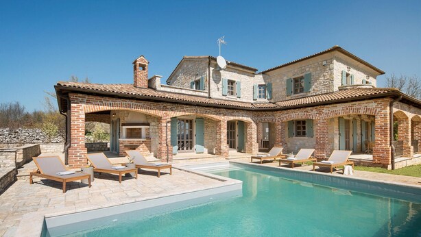 Un'ampia casa con piscina, area relax esterna e facciata in pietra.